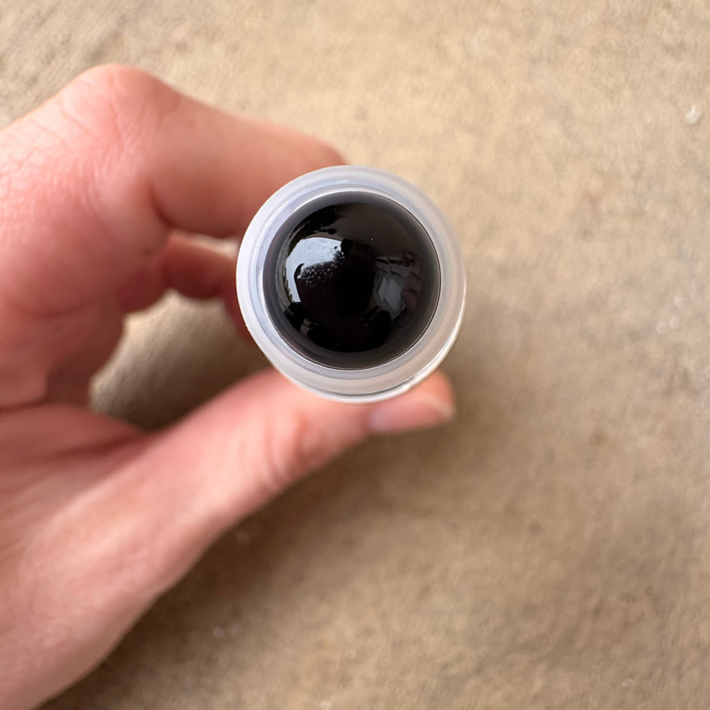 hand holding a roller bottle that shows an upclose obsidian rollerball 