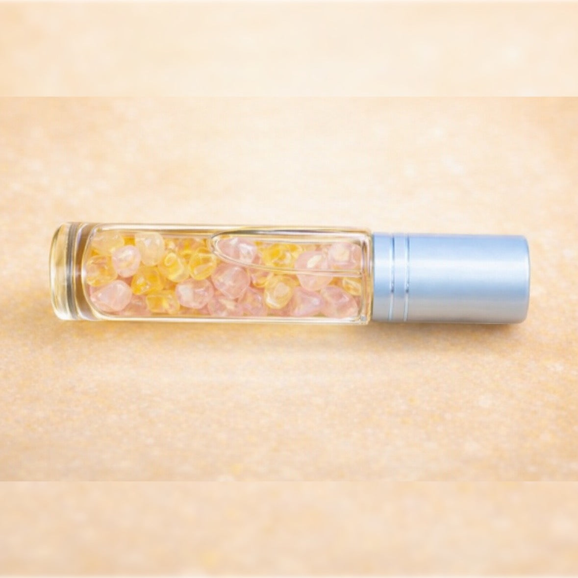 10 ml clear roller bottle with silver cap close up of citrine & rose quartz inside bottle thats laying on its side 